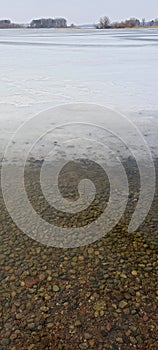 Frozen lake shore water, ice and stones beautiful texture background, march nature landscape