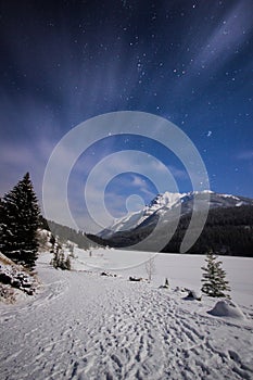 Frozen lake and snowy path in mountains during cold night under sky full of stars and faslty flowing clouds, Two Jack Lake, Banff,
