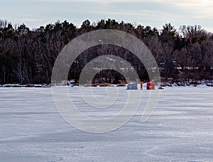 Ice fishing; Frozen lake surface in winter with two ice shanties or huts and a fisherman in between them. photo