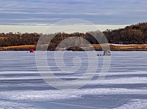 Ice fishing; frozen lake surface in winter with two ice shanties or huts on the frozen lake.