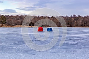 Ice fishing; Frozen lake surface in winter with two ice shanties on the frozen lake surface.  photo