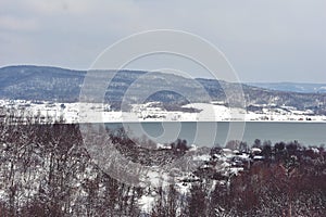 Frozen lake in winter season close to the village with forest reflecting in water