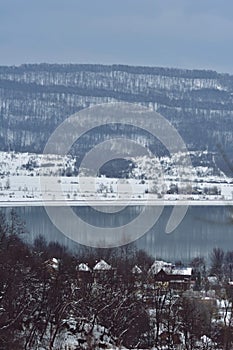 Frozen lake in winter season close to the village with forest reflecting in water