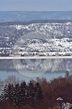 Frozen lake in winter season close to the village with forest reflecting in water