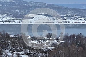 Frozen lake in winter season close to the village with forest reflecting in water