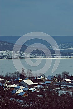 Frozen lake in winter season close to the village with forest reflecting in water