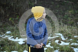 Frozen little thin caucasian girl in yellow hoodie and blue jacket shiver near snow on ground in outdoor park during leisure