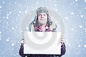 Frozen man with his eyes closed in winter clothes holds a white banner in his hands, there is snow on a blue background around