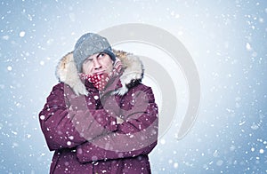 Frozen man in red winter clothes warms his hands and looks up at the sky. Cold, snow, frost, blizzard background