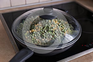 Frozen mix of vegetables in a frying pan on the stove. Close-up
