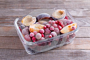 Frozen mixed fruits-berries in a glass container on a wooden table