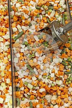 Frozen mixed vegetables with iron scoop in refrigerator in store. Vegetarianism and healthy eating. Close-up