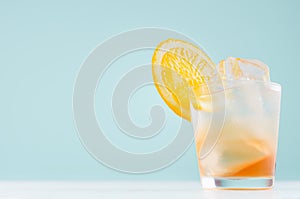 Frozen oranges alcohol drink with orange liquor, sliced fruit, ice cubes in misted shot glass on  blue pastel background.