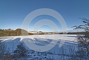 A Frozen over Loch Clunie on a Winters evening with long shadows over the ice covered loch.