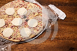 Frozen pizza in an open package on a wooden background. Semifinished. Preparing to cook fast food