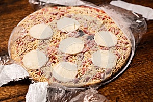 Frozen pizza in an open package on a wooden background. Semifinished. Preparing to cook fast food