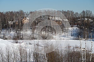 Frozen pond embankment and rural houses in a birch grove, winter background