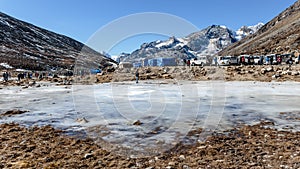 Frozen pond with tourists and market with Yunthang Valley in the background in winter in Zero Point at Lachung. North Sikkim.