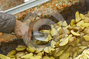 Frozen potato wedges in a refrigerator in a store. A woman\'s hand scoops a product into an iron scoop. Close-up