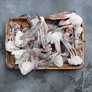 Frozen raw blue swimming crab claws, on wooden tray, on gray background