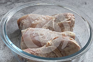 Frozen raw chicken defrosting in a glass dish.