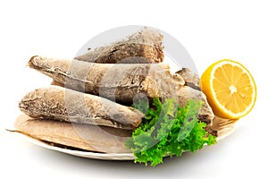 Frozen raw fish hake, pollock on the plate with lemon and leaves of salad lettuce isolated on white background