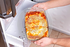 Frozen ready meals. Man`s hands are taking frozen lasagna from the freezer. Concept of storing ready made dinner and saving time