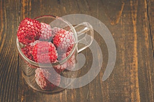 frozen red raspberry in a glass cup /frozen red raspberry used in a glass cup on a wooden table, top view and copyspace