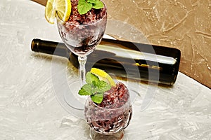 frozen red wine in two glass glasses decorated with a slice of lemon and lemon leaves and an empty glass bottle