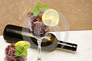 Frozen red wine in two glass glasses decorated with a slice of lemon and lemon leaves and an empty glass bottle