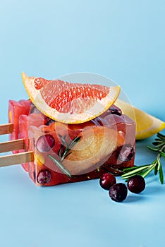 Frozen Refreshing Summer Cocktail Popsicles Recipe Cold Sweet Berry and Citrus Tea with Rosemary Blue Background Vertical