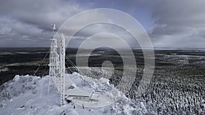 Frozen repeater antenna on the top of a hill in winter. Clip. Aerial view of winter valley panorama and blue cloudy sky.
