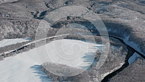 A frozen river flows between the trees covered with white snow. On a frosty sunny December day, spruce trees grow