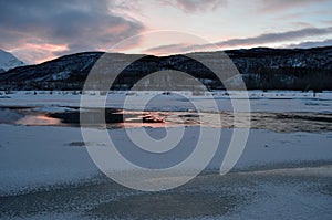 Frozen river landscape with sunny pink glow and reflection