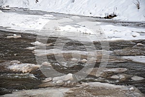 Frozen river in winter, snow and ice melting with fallen trunk of a tree