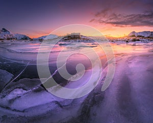 Frozen sea coast and house at colorful sunset in Lofoten islands