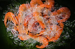 Frozen shrimp with ice cubes on a wood background