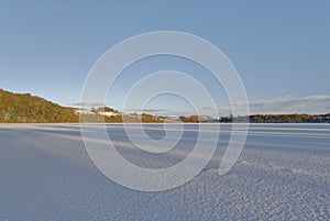 A Frozen and Snow covered Loch Clunie with long shadows across the Loch surface