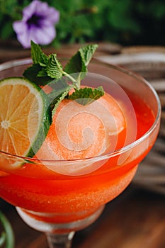 Frozen strawberry Margarita cocktail close-up next to flowers on wooden background