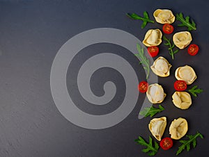 Frozen tortellini on the black background. Italian tortellini with fresh ricotta leaves and tomatoes on a black stone board.