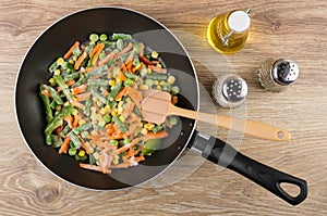 Frozen vegetable mix in frying pan, bottle of oil, spices