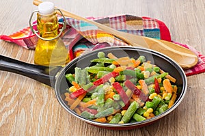 Frozen vegetable mix in frying pan, bottle of vegetable, spoon