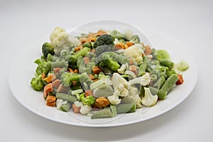 Frozen vegetables: cauliflower, green peas, leeks, broccoli, carrots, green beans on a white plate