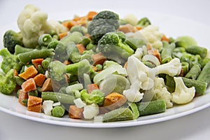 Frozen vegetables: cauliflower, green peas, leeks, broccoli, carrots, green beans on a white plate