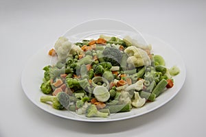 Frozen vegetables: cauliflower, green peas, leeks, broccoli, carrots, green beans on a white plate