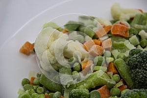 Frozen vegetables: cauliflower, green peas, leeks, broccoli, carrots, green beans on a white plate