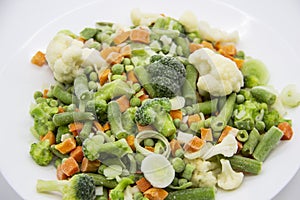 Frozen vegetables: cauliflower, green peas, leeks, broccoli, carrots, green beans on a white plate