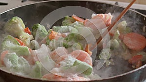 Frozen vegetables are cooked in a frying pan, highlighting steam.