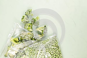 Frozen vegetables. Green peas and broccoli in a transparent bags on a light green background with copy space