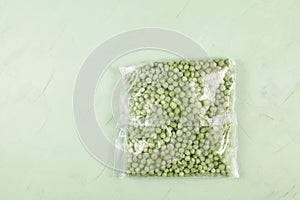 Frozen vegetables. Green peas in a transparent freezer bag. Light green background, copy space